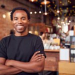 Portrait Of Male Coffee Shop Owner Standing By Counter