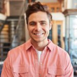 Portrait Of Smiling Male Owner Of Fashion Store Standing In Front Of Clothing Display